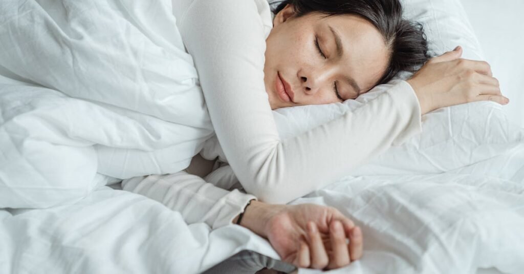 Why Use a Pillow for Better Health Calm Asian female wearing white pajama sleeping in comfortable bed with white sheets near modern mobile phone in morning