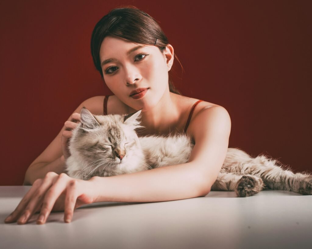 A young woman lovingly cuddles a fluffy cat against a warm red background.